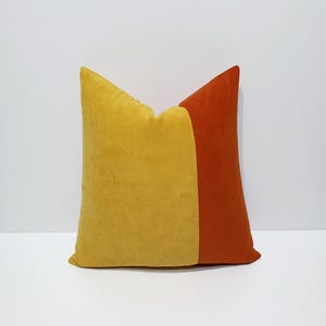 May include: A square throw pillow featuring a color-blocked design with a large mustard yellow section on the left and a smaller burnt orange section on the right. The fabric has a soft, matte, suede-like texture throughout the entire surface.