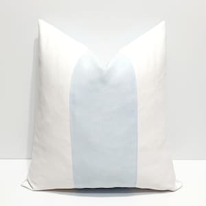 May include: A square throw pillow featuring a solid white fabric on the left and right sides, with a wide, vertical light blue panel centered across the middle. The pillow has a smooth, matte texture and a clean, symmetrical design.