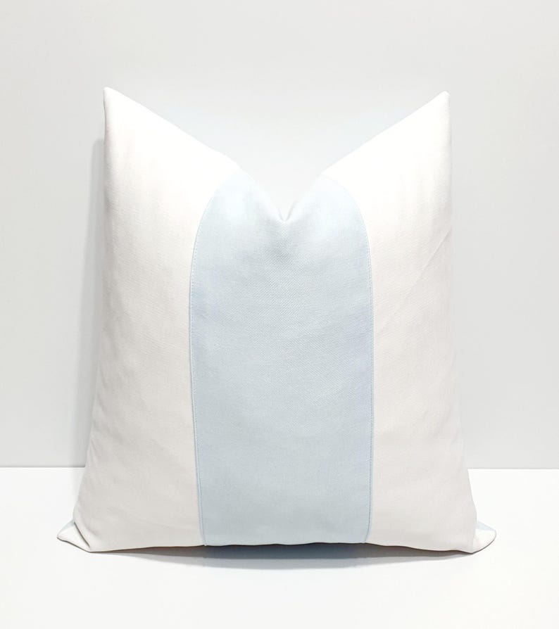 May include: A square throw pillow featuring a solid white fabric on the left and right sides, with a wide, vertical light blue panel centered across the middle. The pillow has a smooth, matte texture and a clean, symmetrical design.