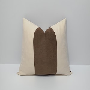 May include: A square throw cushion featuring a colour-blocked design with a wide, central vertical panel in a textured dark brown fabric, flanked by two side panels in a smooth, solid off-white fabric, creating a clean and symmetrical appearance.