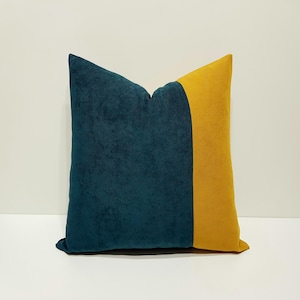Pode incluir: Uma almofada quadrada com um design de blocos de cor, apresentando uma grande secção de tecido com textura aveludada em azul-petróleo escuro à esquerda e um painel vertical de tecido aveludado amarelo-mostarda liso no lado direito da almofada.