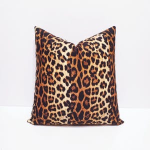 May include: A square throw pillow featuring a prominent leopard print pattern. The design consists of black and dark brown rosettes set against a warm tan and golden-yellow background, covering the entire front surface of the fabric cushion.