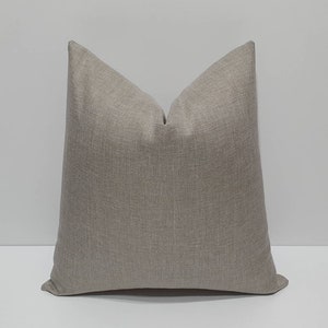May include: A large, square decorative pillow in a neutral taupe color. The pillow has a textured fabric and a simple, modern design, suitable for a living room or bedroom. The pillow is placed against a white background.