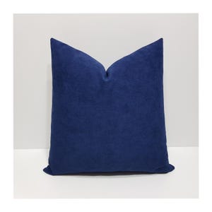 May include: A square throw pillow featuring a solid deep navy blue color with a soft, suede-like texture. The pillow has a distinct pinched top center, creating a structured, upright shape with clean, sharp edges along the sides and bottom.