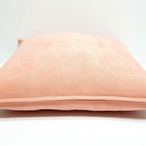 May include: A square throw pillow cover in a solid light peach color. The fabric has a soft, matte texture and features a visible metal zipper closure along the bottom edge, allowing for easy removal and insertion of a pillow insert.