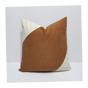 May include: A square throw pillow featuring a color-blocked design with a large, central brown section and two off-white triangular corners. The fabric has a soft, matte texture, and the pillow is constructed with clean, straight seams.