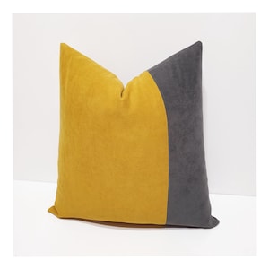 May include: A square throw pillow featuring a color-blocked design with a large mustard yellow section on the left and a dark charcoal gray section on the right. The fabric has a soft, matte texture, and the two colors are joined by a curved seam.