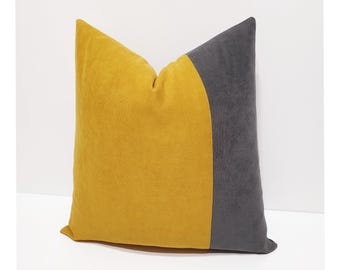 May include: A square throw pillow featuring a color-blocked design with a large mustard yellow section on the left and a dark charcoal gray section on the right. The fabric has a soft, matte texture, and the two colors are joined by a curved seam.