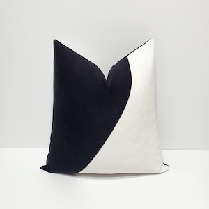 May include: A square throw cushion featuring a bold, two-tone design. The left side is solid black, while the right side is solid white, divided by a curved, sweeping line that creates a distinct contrast across the front of the cushion cover.