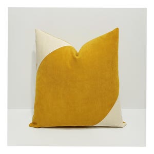 May include: A square throw pillow featuring a bold, diagonal color-blocked design. The pillow is primarily mustard yellow with two contrasting off-white triangular corners at the top left and bottom right, finished in a soft, velvet-like texture.