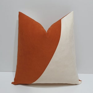 May include: A decorative throw pillow with a geometric design. One side is a burnt orange color and the other side is a cream color.