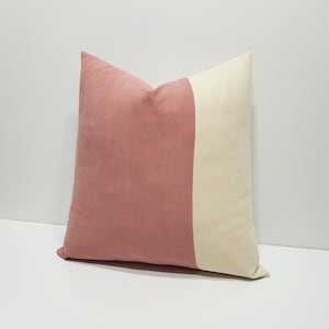 Puede incluir: Una almohada de tiro de color rosa y crema con un diseño geométrico. La almohada está hecha de una tela suave y mullida.