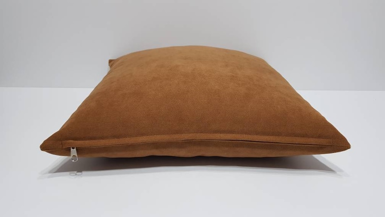 May include: A brown suede pillow with a zipper closure.