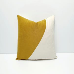 May include: A square throw pillow featuring a color-blocked design. The left side is a deep mustard yellow fabric with a visible woven texture, while the right side is a smooth, solid off-white fabric divided by a diagonal seam across the center.
