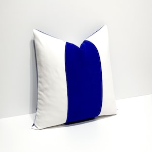 Puede incluir: Una almohada de tiro a rayas blancas y azul real. La almohada está hecha de una tela suave y mullida y tiene un diseño simple y moderno.