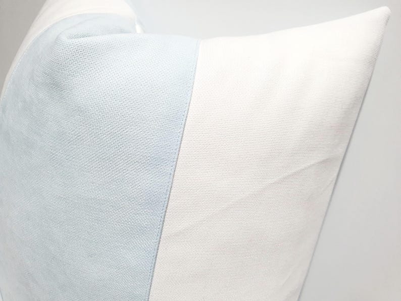 May include: A square throw pillow featuring a color-blocked design with a vertical panel of light blue textured fabric on the left side and a larger panel of solid white fabric on the right side, showcasing a clean and simple aesthetic.