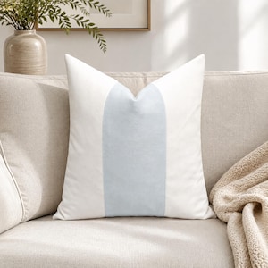 May include: A square throw pillow featuring a vertical color-blocked design. The pillow has a wide, central panel in a soft, pale blue hue, flanked on both the left and right sides by solid white panels. The fabric appears smooth and uniform.