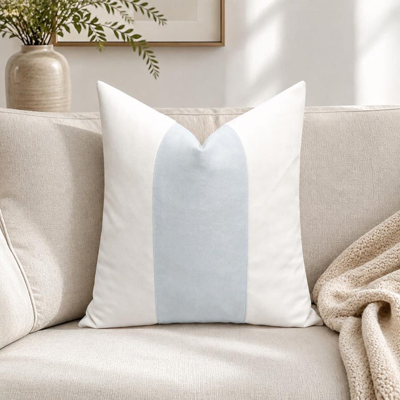 May include: A square throw pillow featuring a vertical color-blocked design. The pillow has a wide, central panel in a soft, pale blue hue, flanked on both the left and right sides by solid white panels. The fabric appears smooth and uniform.