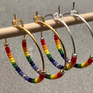May include: Three pairs of hoop earrings with rainbow colored beads. The hoops are made of gold and silver metal.