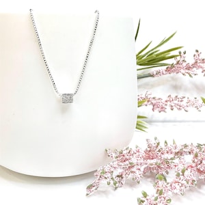 May include: A silver chain necklace with a small, textured, square pendant.