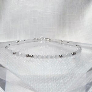 Puede incluir: Un delicado brazalete de cuentas blancas con cuentas espaciadoras plateadas. El brazalete está hecho con cuentas facetadas y tiene un cierre plateado.