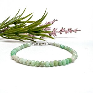 May include: A green gemstone bracelet with a silver clasp. The bracelet is made of small, faceted beads that are graduated in size, with the larger beads at the center of the bracelet.