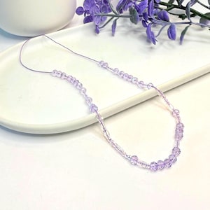 May include: A delicate necklace featuring light purple, translucent, faceted beads strung on a thin, flexible cord. The beads are arranged in a repeating pattern of small round shapes interspersed with slightly longer, cylindrical, clear-tinted pieces.