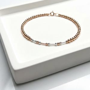 Puede incluir: Una pulsera delicada que presenta una hebra continua de pequeñas cuentas de oro rosa intercaladas con una secuencia de barras cilíndricas y cuentas esféricas de plata y oro rosa, asegurada con un pequeño cierre de resorte circular.