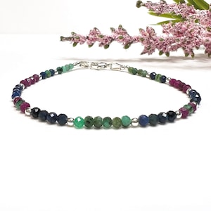 May include: A delicate bracelet featuring a gradient of gemstones, including ruby, sapphire, and emerald, interspersed with silver beads.