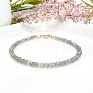 May include: A delicate bracelet made with small, faceted labradorite beads in shades of gray and blue. The bracelet has a gold-toned clasp.