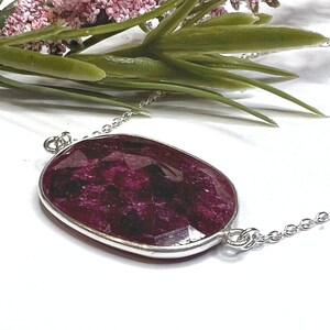 May include: A silver chain necklace with a large, oval-shaped, faceted ruby pendant.