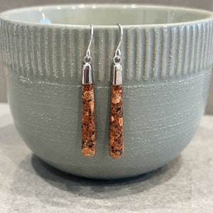 May include: A pair of silver dangle earrings with brown and orange speckled stone accents.