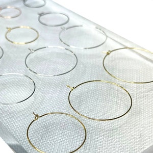 May include: Assortment of hoop earrings in various sizes and finishes, including gold, silver, and rose gold. The hoops are displayed on a white surface.