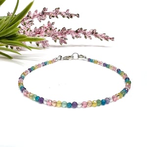 May include: A delicate bracelet made with small, colorful beads in shades of pink, green, blue, and purple. The bracelet is made with a silver clasp.