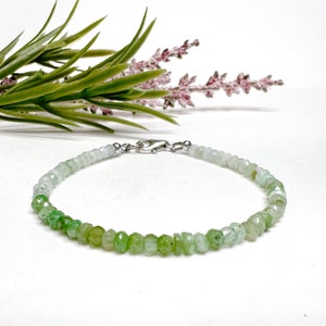May include: A delicate green and white gemstone bracelet with a silver clasp. The bracelet is made of small, faceted beads that are graduated in size, with the larger beads at the bottom. The bracelet is perfect for adding a touch of elegance to any outfit.