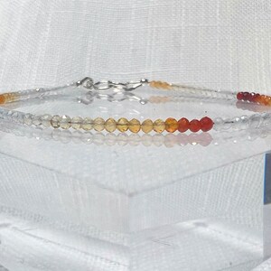 May include: A delicate bracelet with a gradient of clear, yellow, orange, and red beads. The bracelet is made with small, round beads and has a silver clasp.