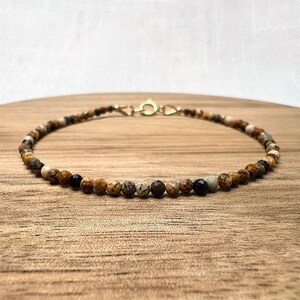 May include: A brown, black, and white gemstone beaded necklace with a gold clasp.