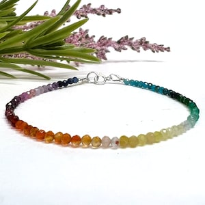 May include: A rainbow gemstone bracelet with a silver clasp. The bracelet features a gradient of colors from purple to green.