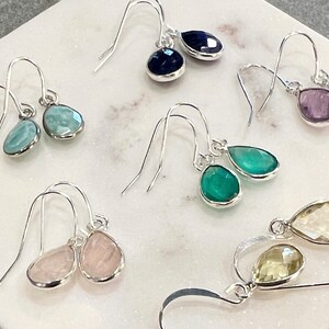 May include: A set of ten silver dangle earrings with teardrop-shaped gemstones in various colors, including blue, green, pink, and purple.