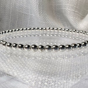 May include: A silver beaded bracelet with a simple design. The bracelet is made of small, round beads that are strung together on a thin wire.