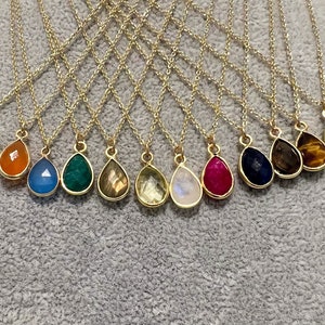May include: A set of 14 gold necklaces with teardrop-shaped gemstone pendants. The gemstones are in various colors, including green, blue, red, orange, brown, and white.