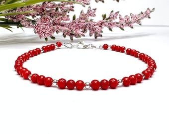 May include: A red coral bead bracelet with a silver clasp. The bracelet is made of small, round beads and is strung on a silver chain.