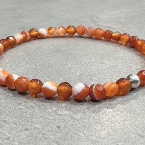 May include: A carnelian bracelet with a silver bead. The carnelian beads are orange and white with a striped pattern.
