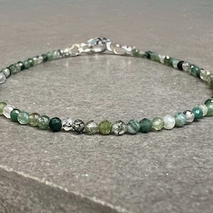 May include: A delicate green agate gemstone bracelet with silver clasp. The bracelet features a variety of green shades and textures.