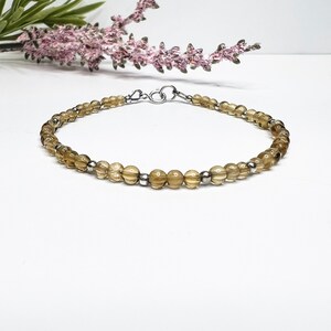 May include: A delicate bracelet made with small, light brown beads and silver accents. The bracelet has a simple, elegant design and is perfect for everyday wear.