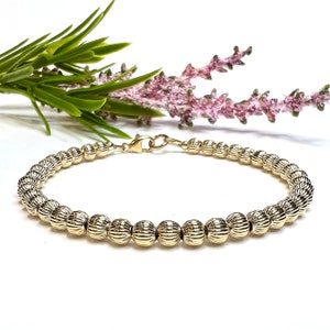 May include: A gold beaded bracelet with a textured design. The bracelet has a lobster claw clasp.