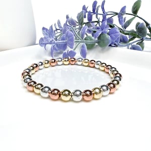 May include: A bracelet made of silver, gold, and rose gold beads. The beads are round and have a smooth finish.