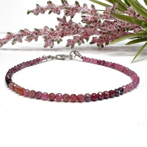 May include: A delicate bracelet made with small, round, pink and purple gemstone beads. The bracelet has a silver clasp.