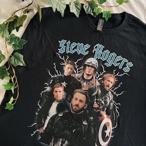 May include: Black t-shirt featuring a graphic of Steve Rogers, with the text "Steve Rogers" in a stylized font. The graphic includes multiple images of the character, with lightning bolt accents. The shirt is a crew neck.
