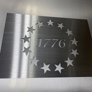 May include: A silver metal plaque with a circle of thirteen stars cut out around the number 1776.